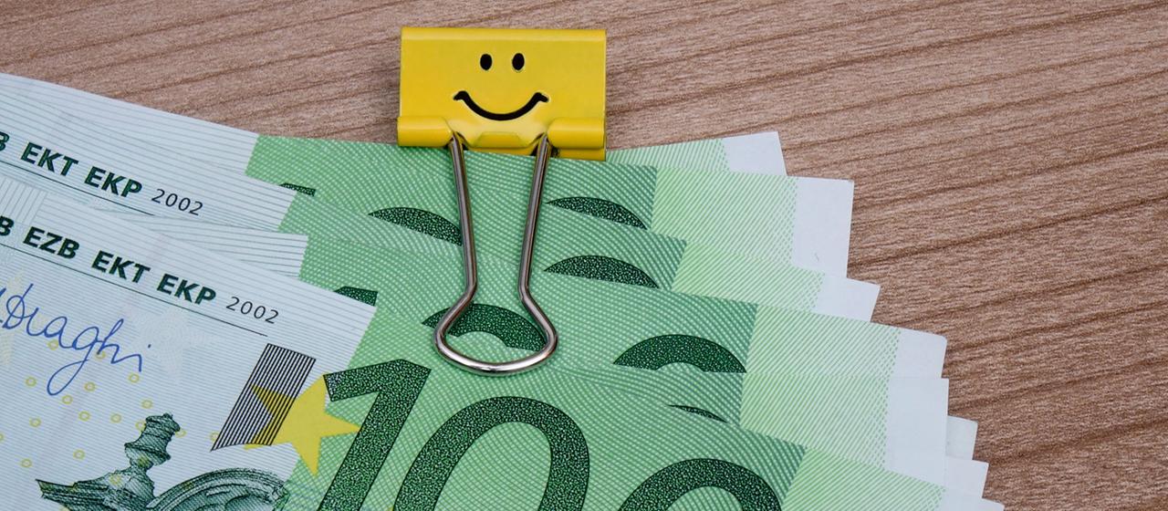 Ein Bündel Geldscheine wird mit einer Geldscheinklammer gehalten.