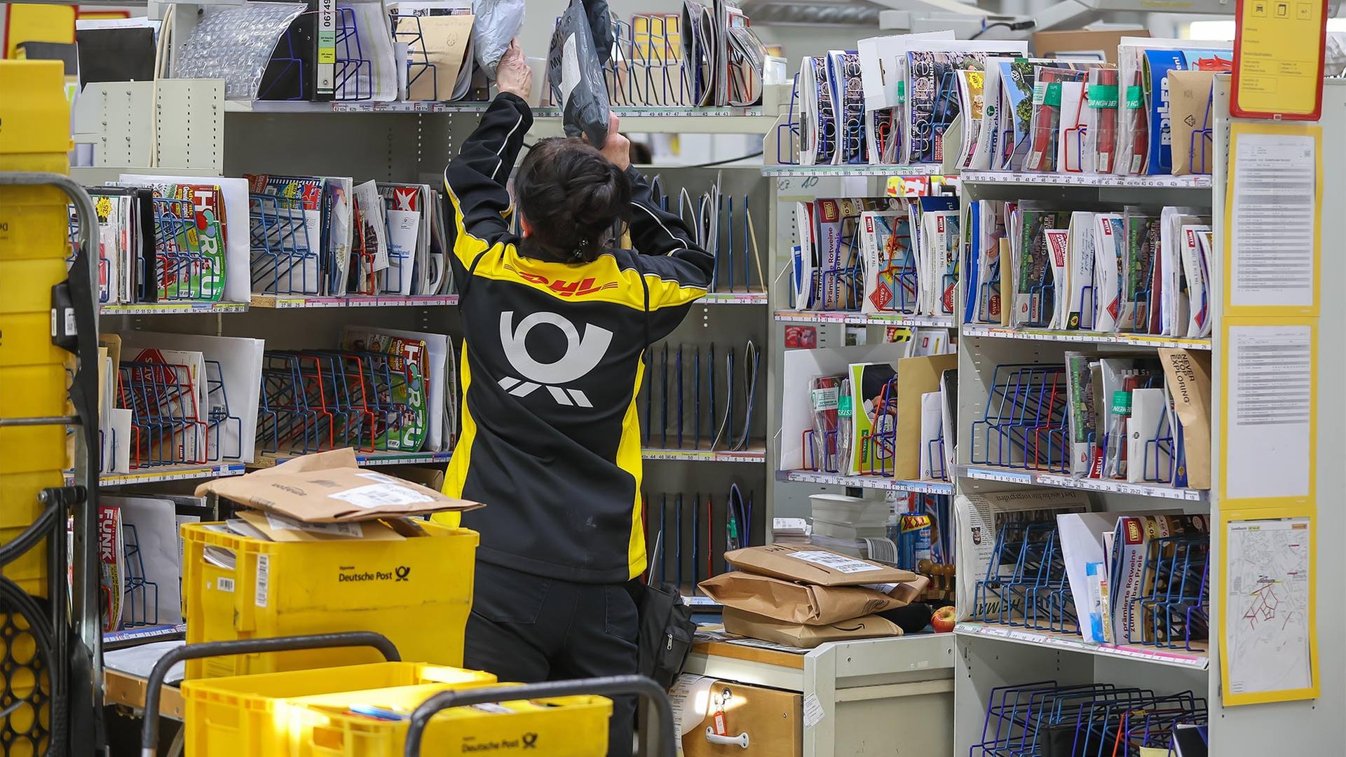 Eine Mitarbeiterin der Deutsche Post DHL sortiert Briefe und Warensendungen.  | picture alliance/dpa
