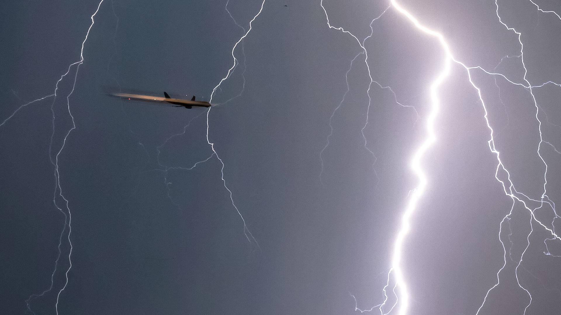 Ein Blitz durchzuckt den Himmel während sich ein Flugzeug im Landeanflug befindet (Archivbild) | picture alliance/dpa