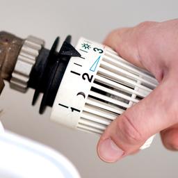 Eine Frau dreht am Thermostat einer Heizung.