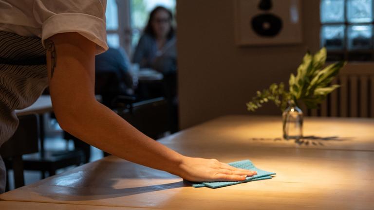 Eine Frau wischt einen Tisch mit einem Tuch ab