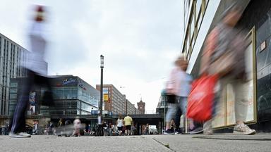 Passanten gehen mit Einkaufstüten durch die Fußgängerzone am Alexanderplatz, Berlin.