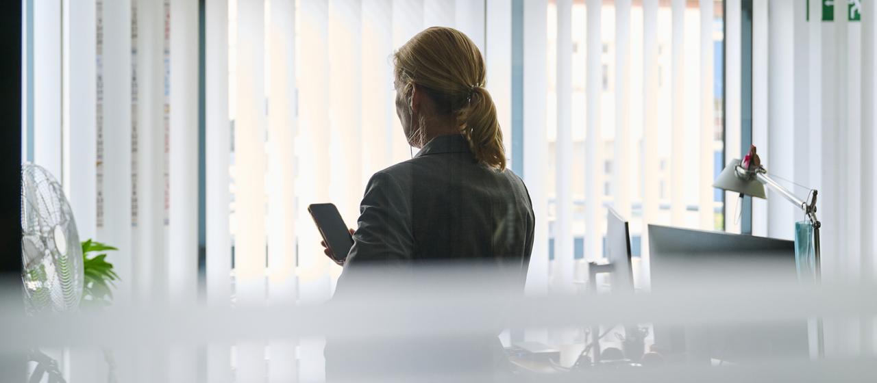 Eine Frau steht in einem Büro am Fenster und telefoniert
