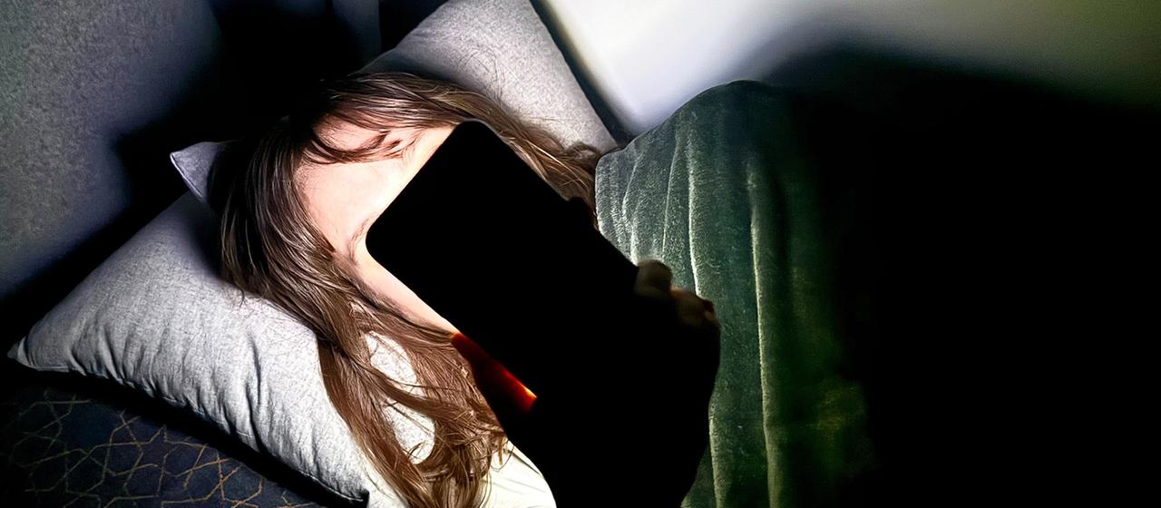 Eine Frau liegt auf einem Sofa und blickt auf ein Handy.