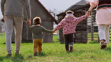 Zwei Kinder gehen Hand in Hand mit zwei Erwachsenen - Symbolbild Familie