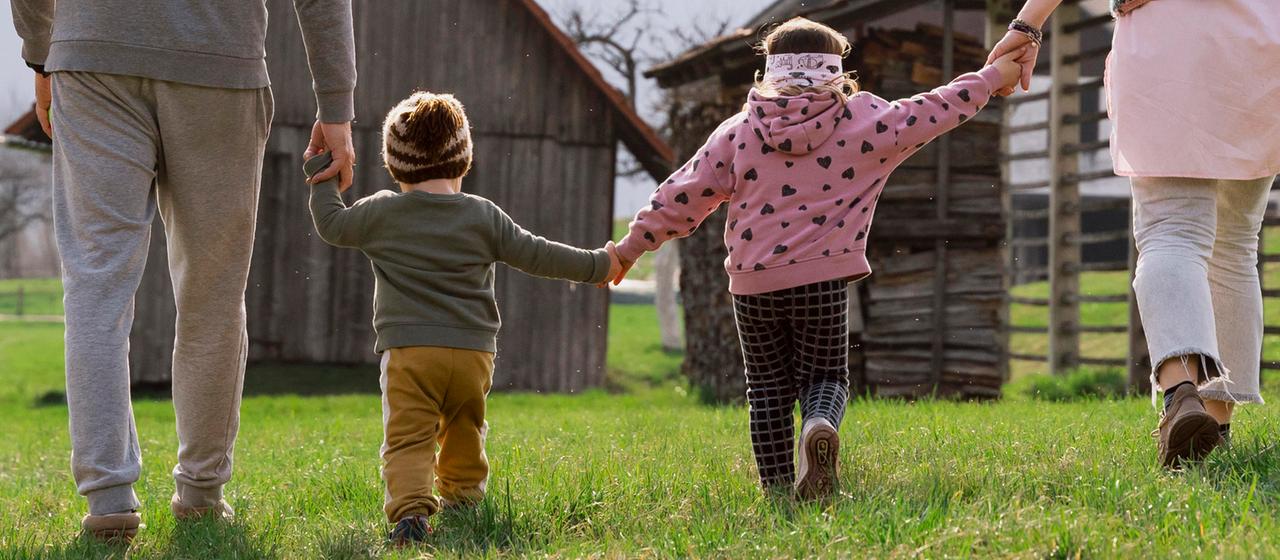 Zwei Kinder gehen Hand in Hand mit zwei Erwachsenen.