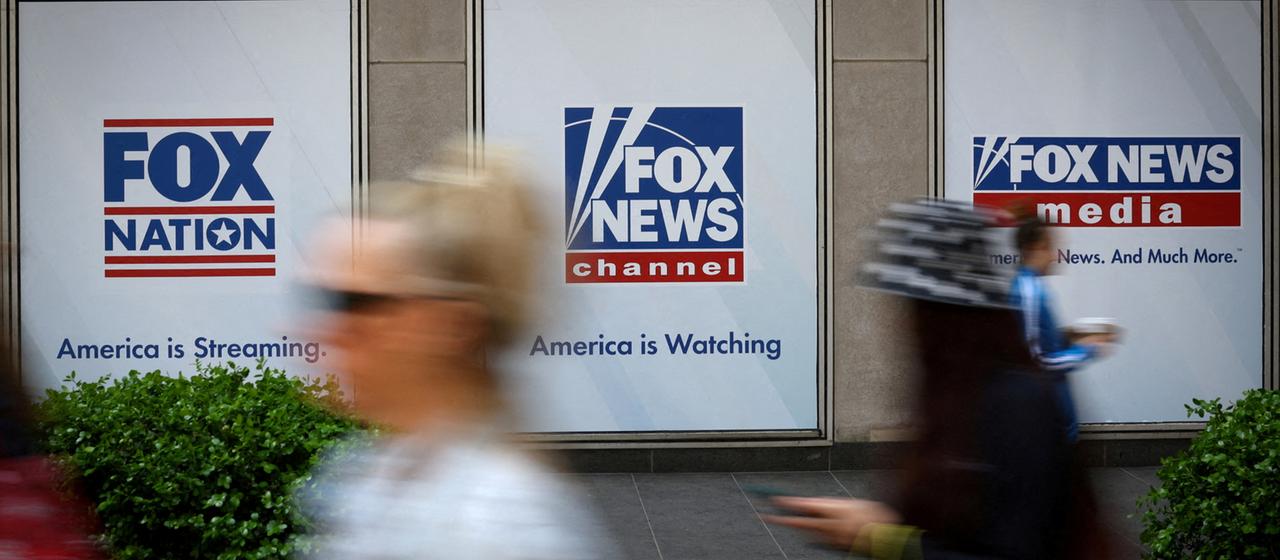 Menschen laufen an Schildern des US-Senders Fox News vorbei.