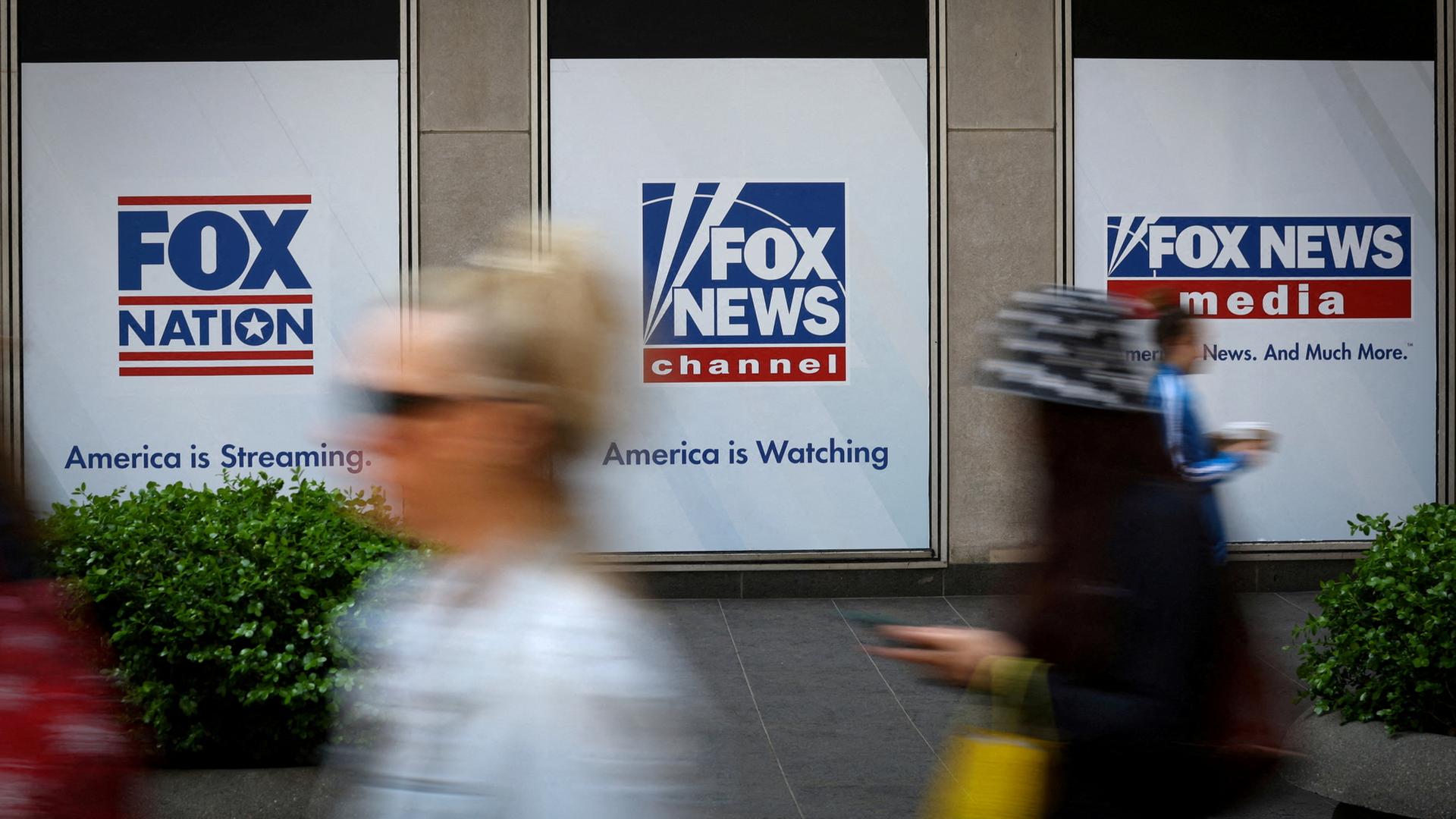 Menschen laufen an Schildern des US-Senders Fox News vorbei. | REUTERS