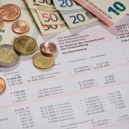 Foto: Geldmünzen und -scheine liegen auf einer Betriebskostenabrechnung