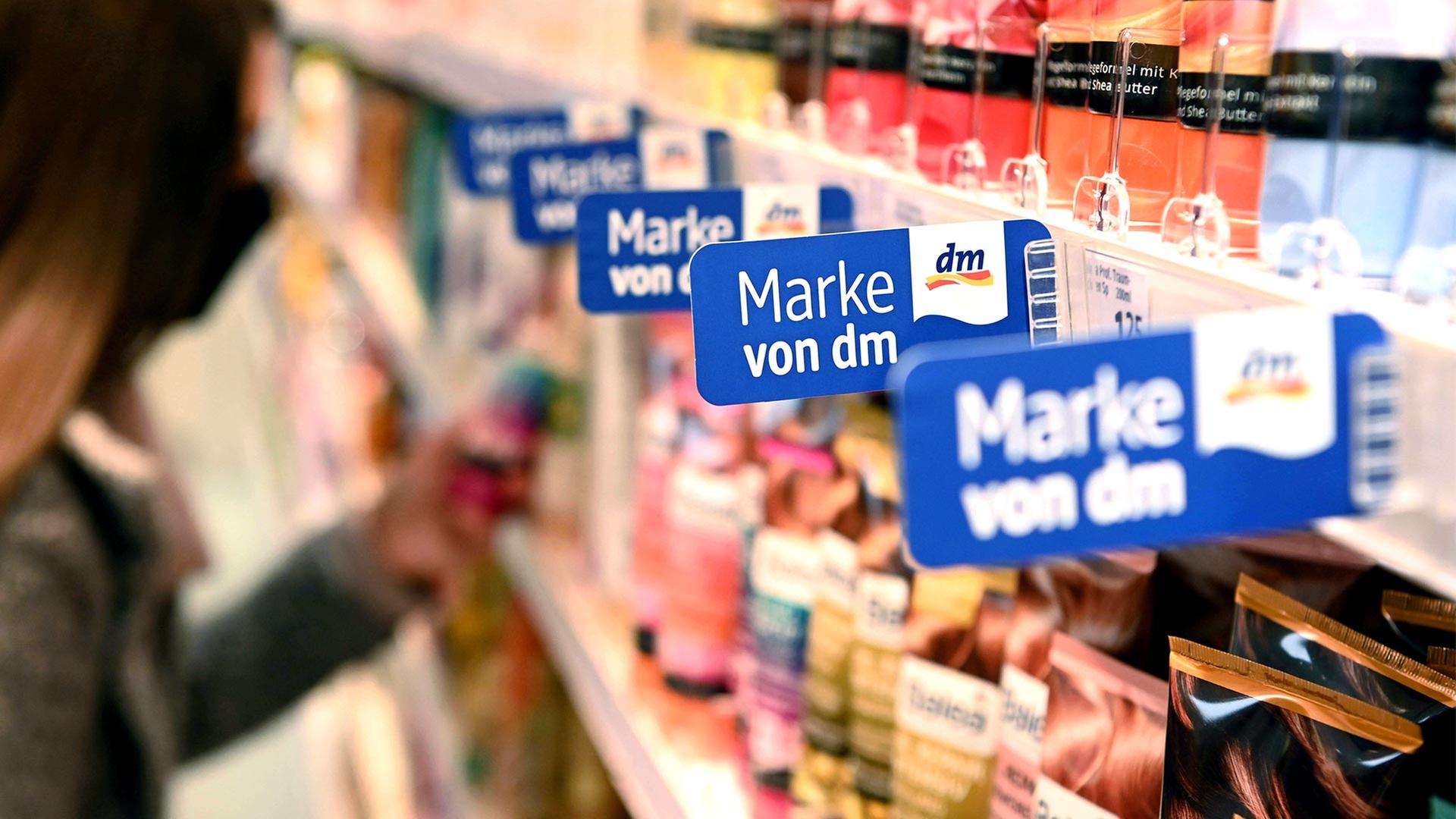 In einem Regal einer Filiale der Drogeriemarktkette dm hängen Schilder, die auf die Eigenmarken hin weisen. | picture alliance/dpa