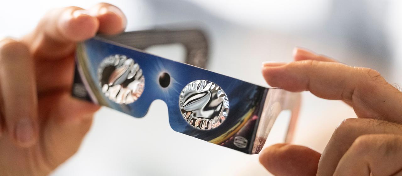 Eine Person hält eine Sonnenfinsternis-Schutzbrille in den Händen.