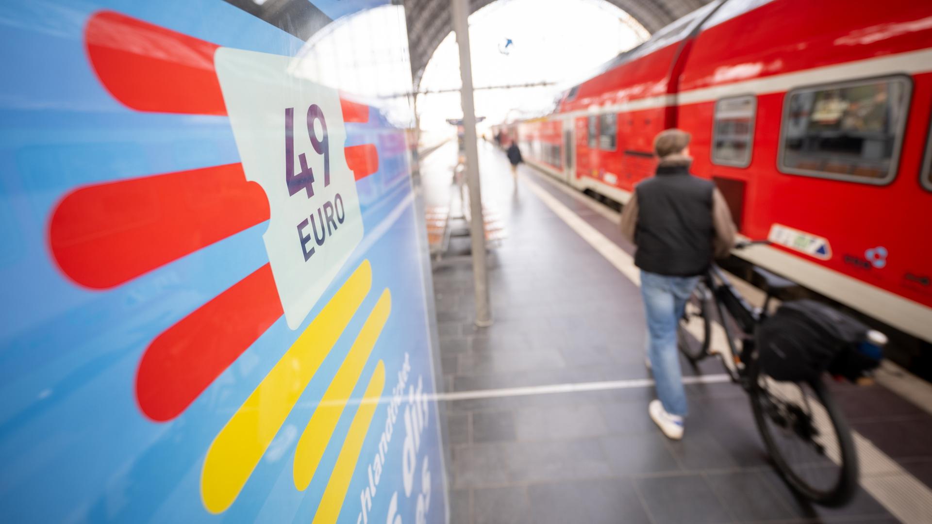 Ein Mann geht am Hauptbahnhof mit seinem Fahrrad zwischen der Werbung für das Deutschlandticket und einer Regionalbahn entlang.