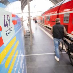 Ein Mann geht am Hauptbahnhof mit seinem Fahrrad zwischen der Werbung für das Deutschlandticket und einer Regionalbahn entlang.