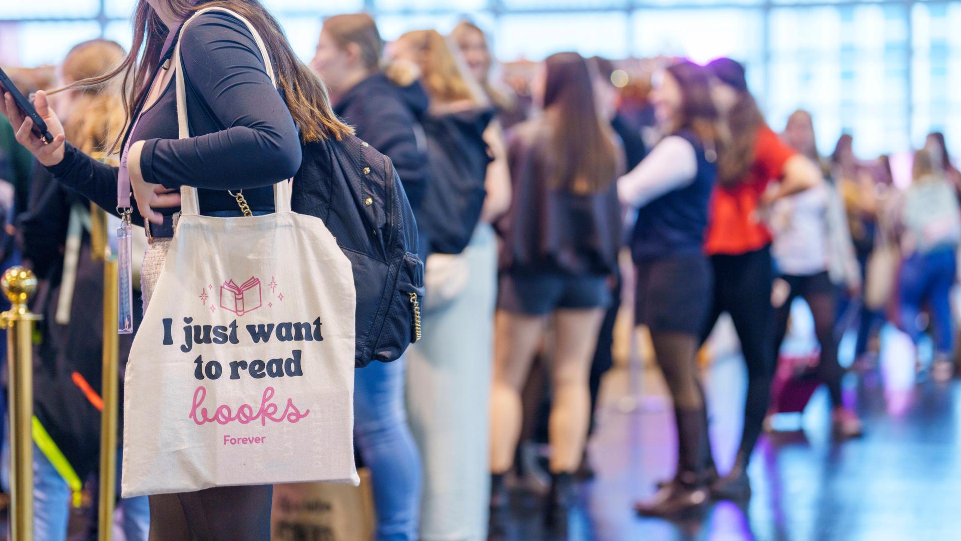 Im Vordergrund links eine Frau, die eine Stofftasche mit der Aufschrift 