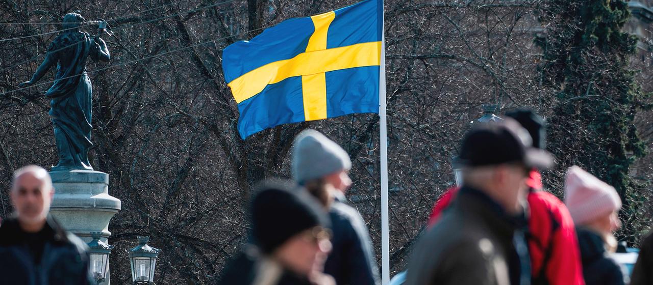 Menschen laufen vor einer schwedischen Flagge entlang.