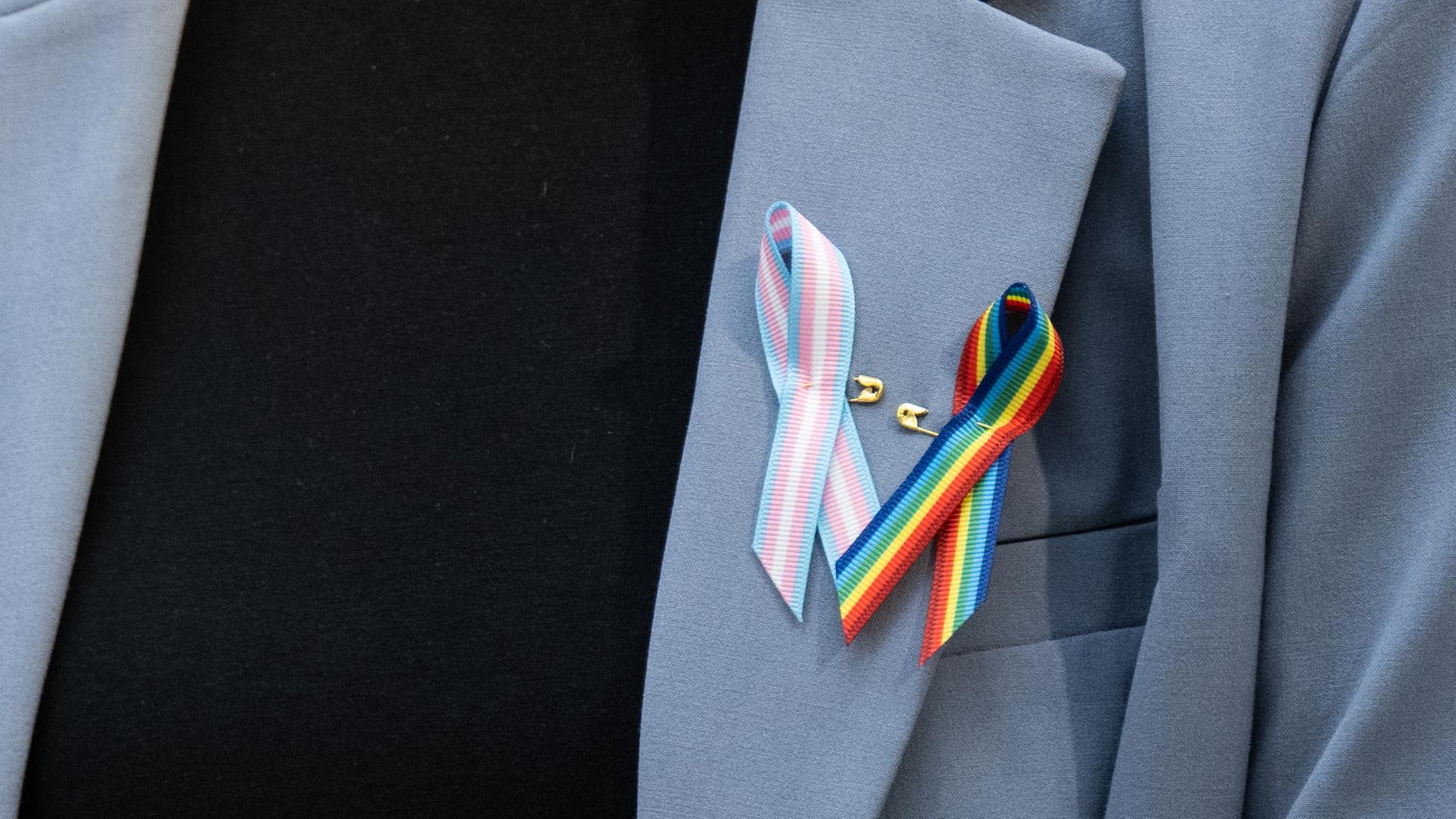 Ein Person trägt Schleifen in den Farben der Transgender und LGBT+ Flagge.  | dpa
