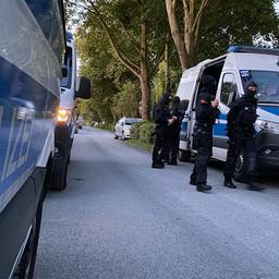 Einsatzkräfte der Polizei stehen neben Polizeifahrzeugen.