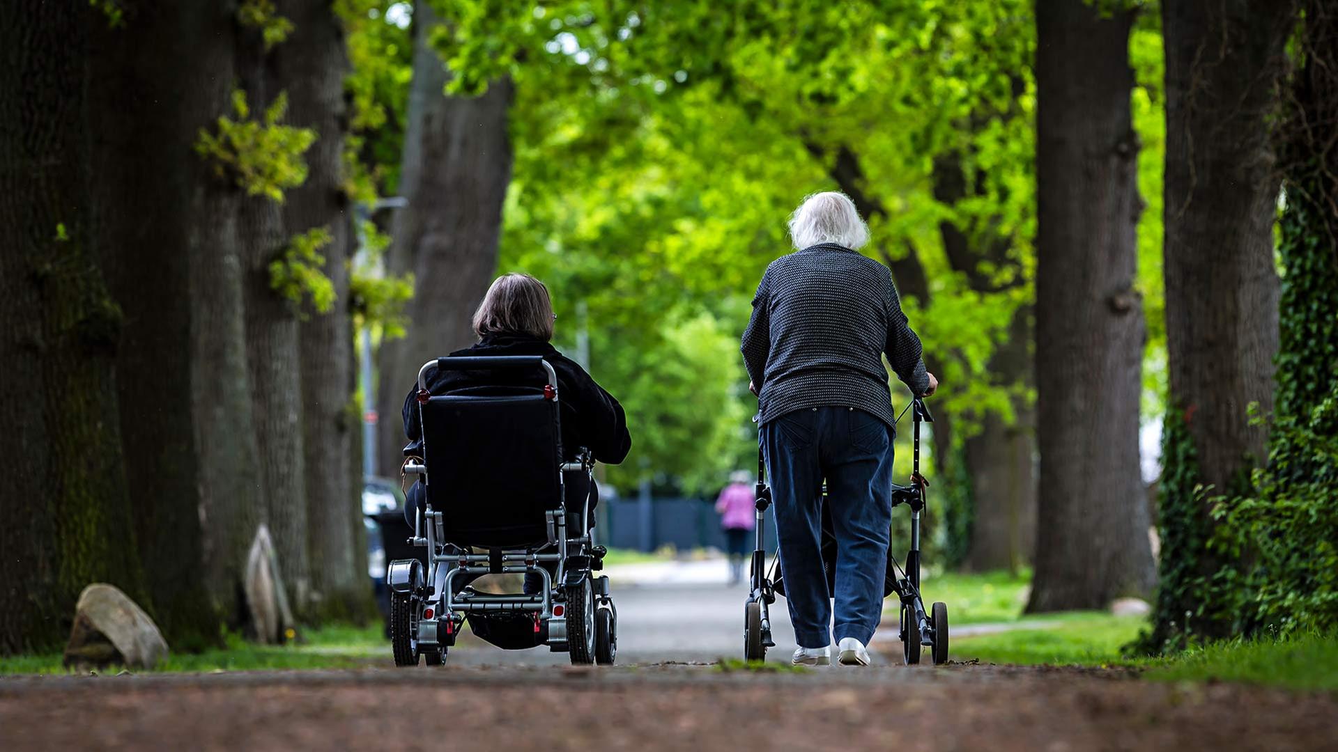 Zwei alte Personen, eine davon im Rollstuhl, die andere mit Rollator. | picture alliance/dpa