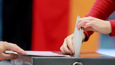 Hände stecken Stimmzettel in eine Wahlurne