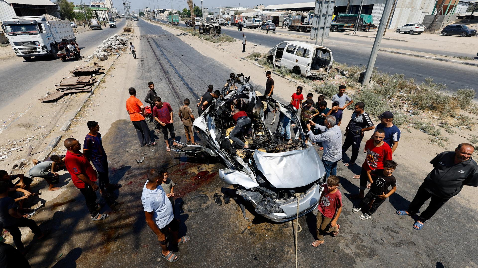 Menschen stehen neben einem zerstörtem PKW im Gazastreifen | REUTERS