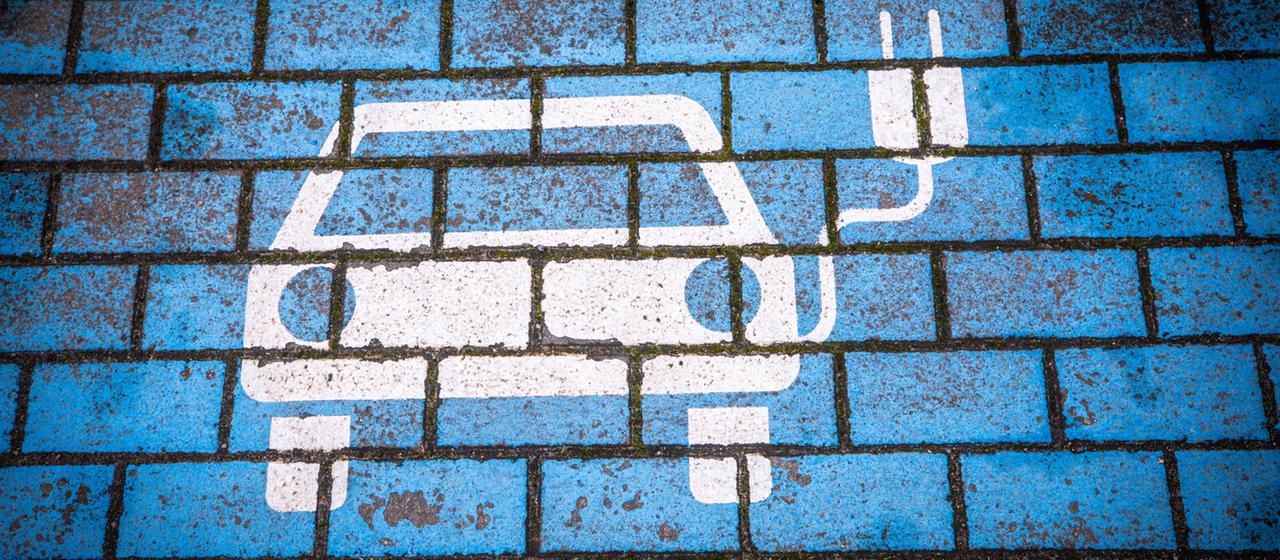 Aufdruck auf Straßenpflaster zeigt ein Elektroauto mit einem Ladekabel