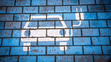 Ein Aufdruck auf Straßenpflaster zeigt ein Elektroauto mit einem Ladekabel.