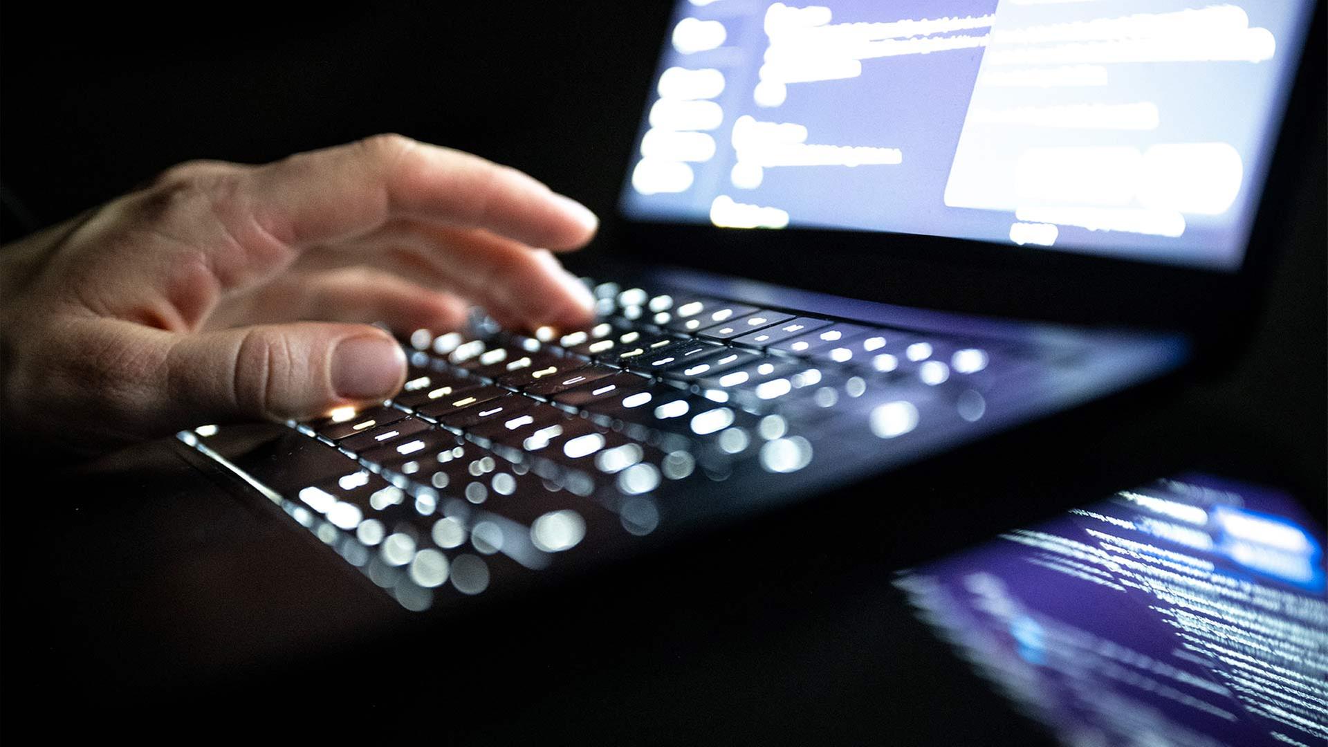 Eine Person tippt auf einer beleuchteten Laptop-Tastatur. | picture alliance/dpa