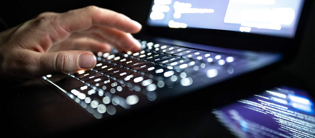 Eine Person tippt auf einer beleuchteten Laptop-Tastatur.