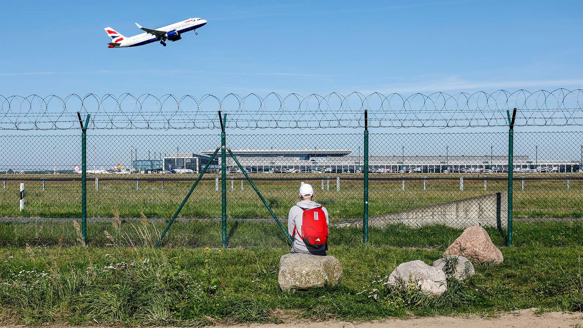 Ein Mann beobachtet durch einen Zaun den Start eines Flugzeugs am Flughafen BER. | picture alliance / Jochen Eckel