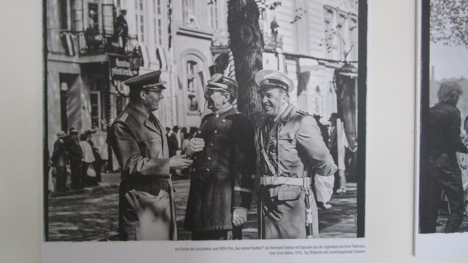 Ein schwarz-weiß Foto zeigt zwei Polizisten und einen Soldaten in Uniform, die auf einer Straße stehen und lachen