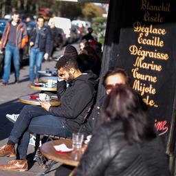 Passanten sitzen in einem Straßencafe in Paris.