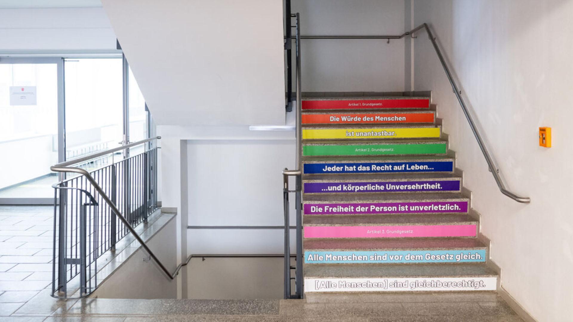 Auf einer Treppe sind am Ludwig-Leichhardt-Gymnasium mit bunten Aufklebern die ersten drei Artikel des Grundgesetzes aufgeklebt. (Quelle: dpa/Gollnow) | dpa/Gollnow