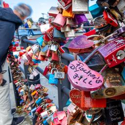 Ein Mann betrachtet sogenannte Liebesschlösser an einem Brückengeländer in Rostock.