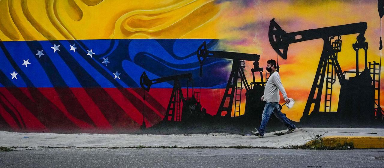 Ein Mann vor einem Wandgemälde mit Ölpumpen und der Flagge Venezuelas.