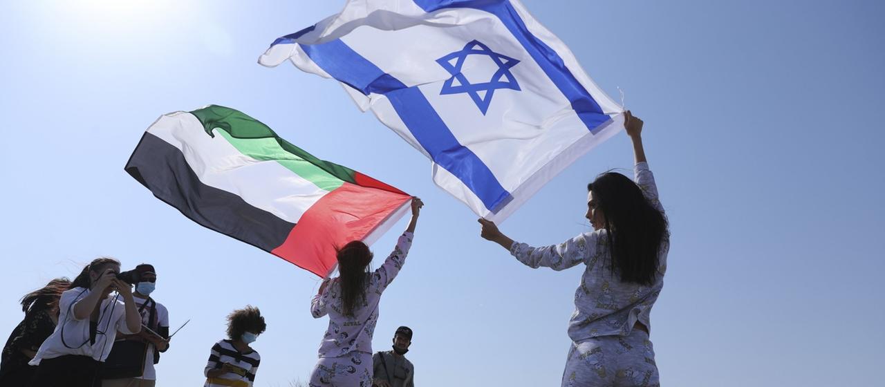Zwei Models halten die Flaggen der Vereinigten Arabischen Emirate und Israels in die Luft