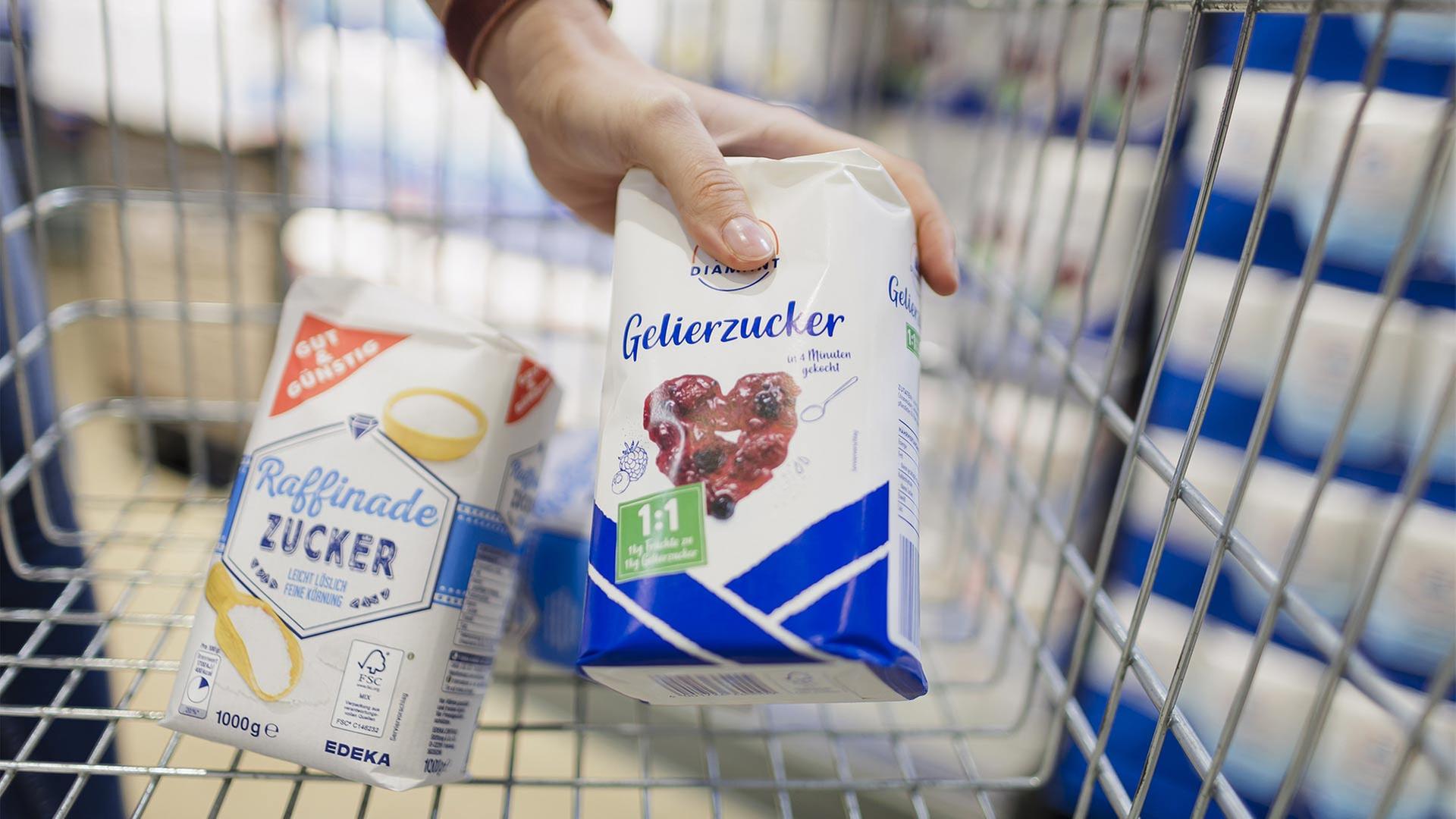 Eine Hand legt Gelierzucker zu einem Paket Zucker in einen Einkaufswagen. | picture alliance / photothek