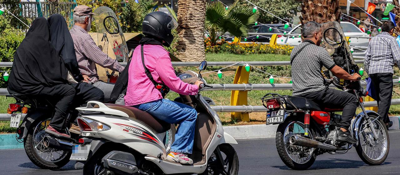 Frauen und Männer auf Motorrollern auf einer Straße in Teheran, Iran.