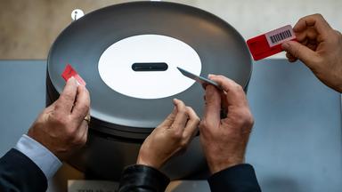 Hände mit Abstimmungskarten an einer Urne im Bundestag