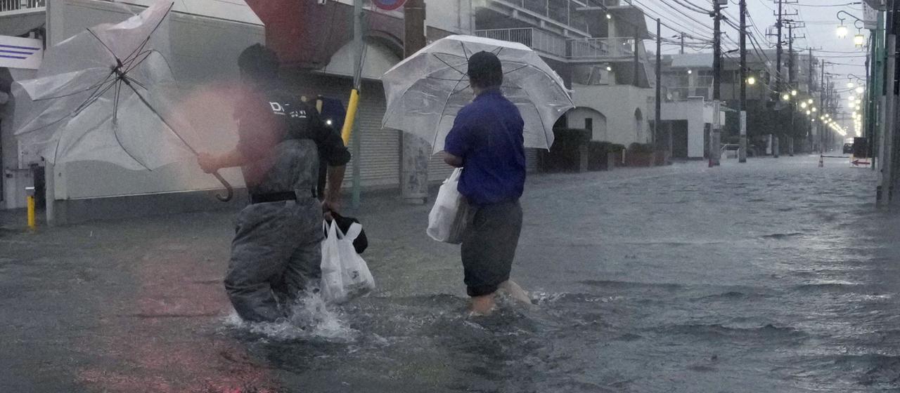 Menschen waten durch eine überflutete Straße, während der Taifun Dujuan in Ichikawa, Japan, heftige Regenfälle bringt.