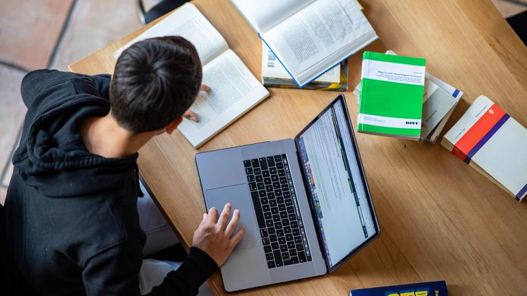 Ein Student vor Büchern und seinem Laptop. 