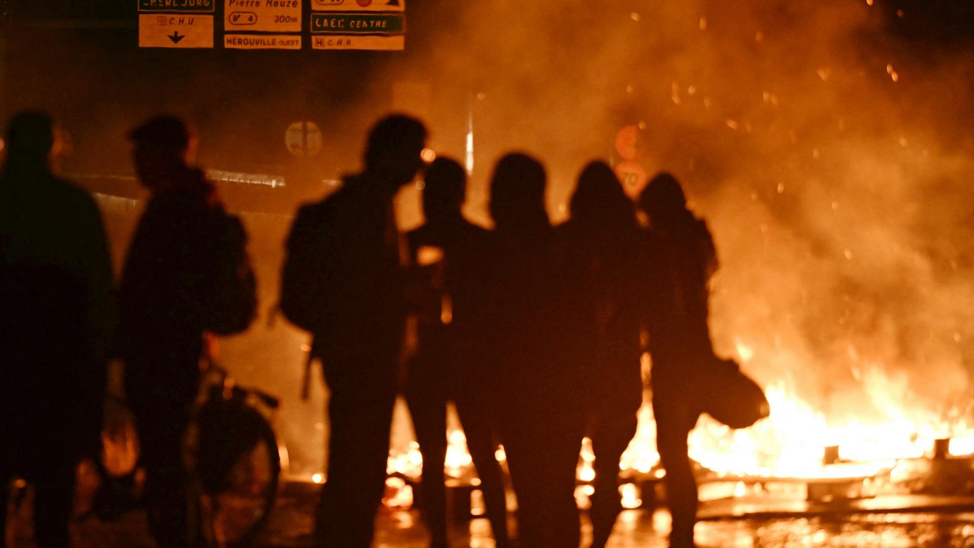 Protestierende der Gruppe Bloquons tout in Frankreich stehen vor Flammen. | AFP