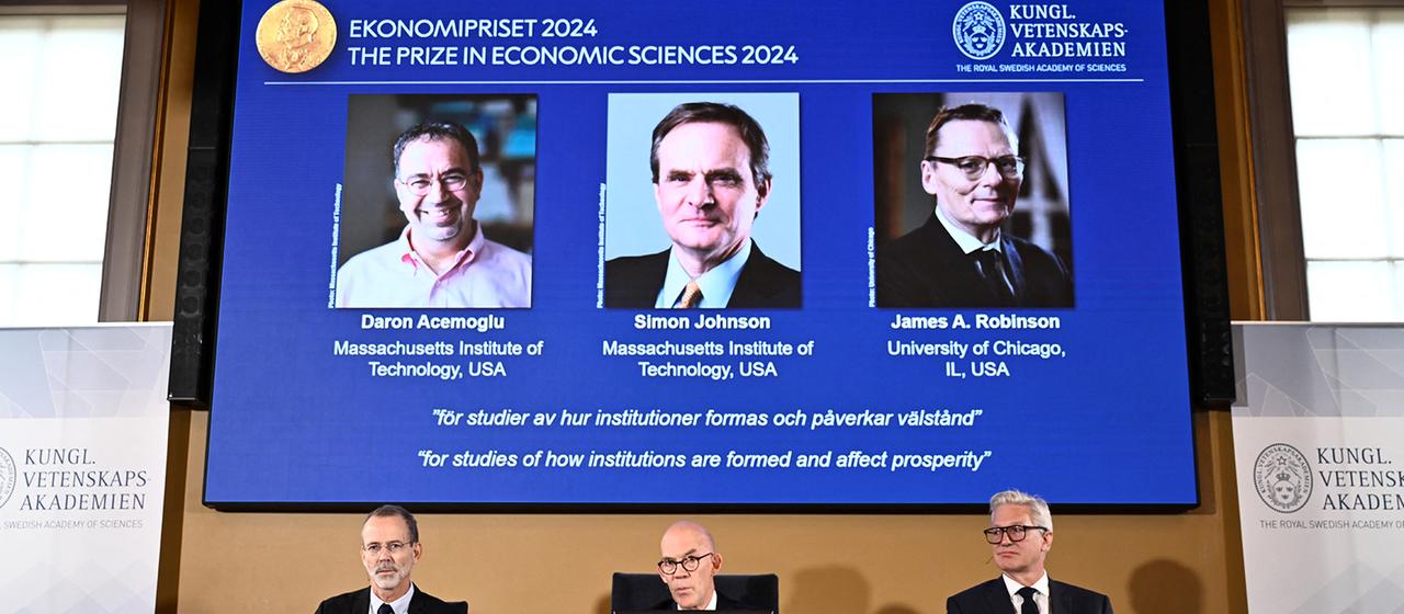 Bei der Bekanntgabe des Wirtschaftsnobelpresies sind auf einem Bildschirm die Fotos von Acemoglu, Johnson und Robinson zu sehen. | via REUTERS Bei der Bekanntgabe des Wirtschaftsnobelpresies sind auf einem Bildschirm die Fotos von Acemoglu, Johnson und Robinson zu sehen.