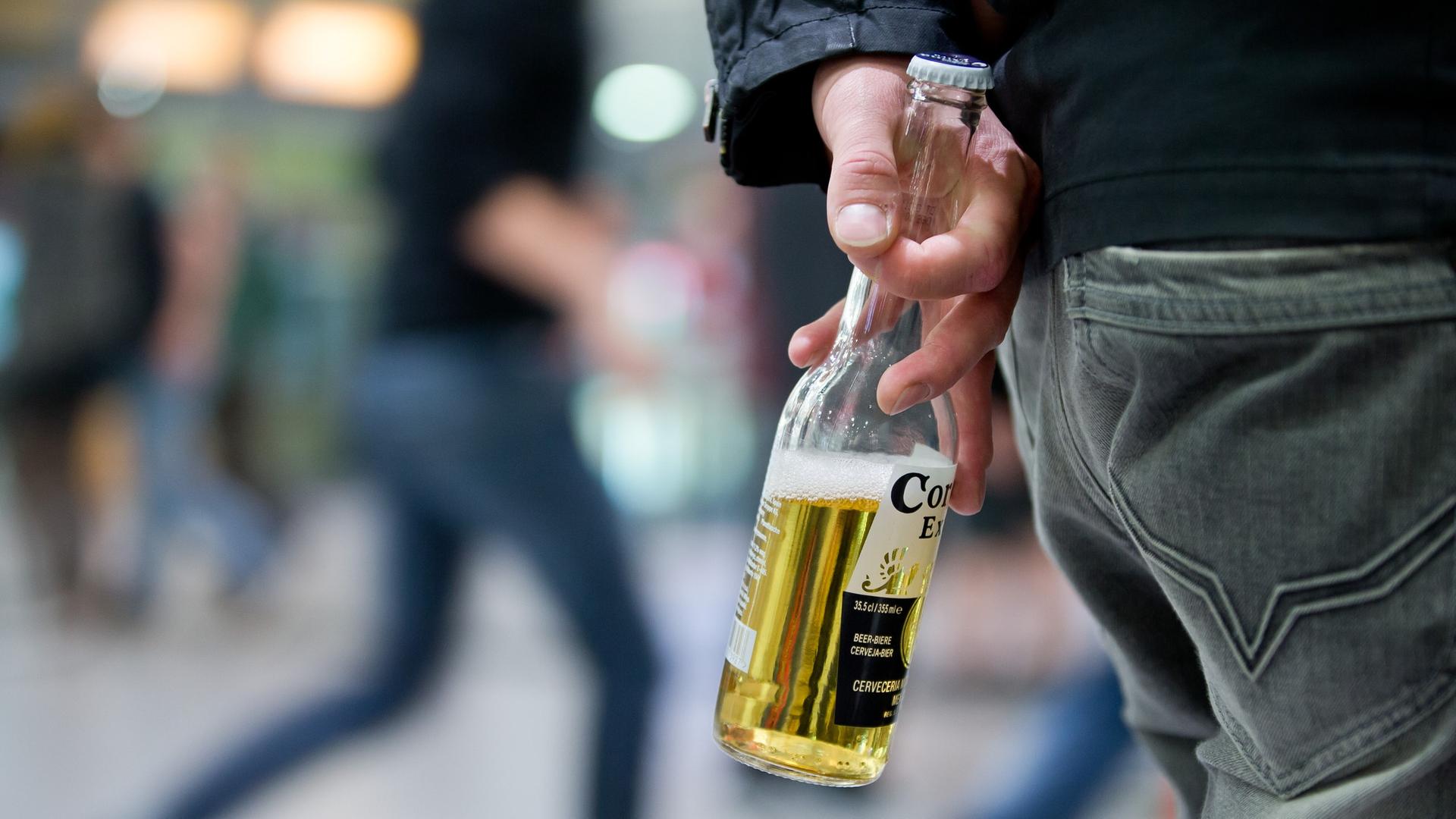 Ein Jugendlicher steht mit einer Flasche Bier in der Hand in einem Bahnhof, im Hintergrund gehen Menschen. | picture alliance / dpa | Daniel Karmann