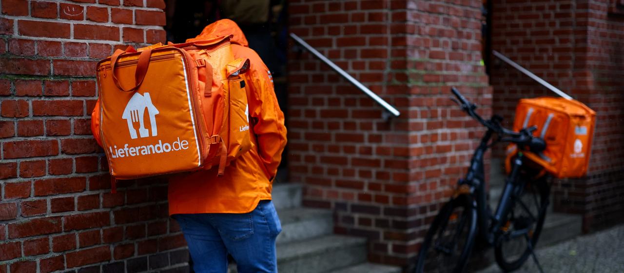 Ein Lieferando-Lieferdienstfahrer steht vor einem Haus in Berlin