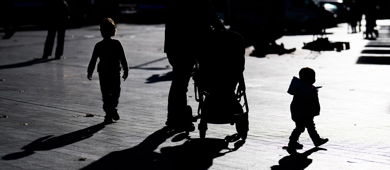 Zwei Kinder und ein Elternteil mit einem Kinderwagen laufen im Gegenlicht der Sonne durch die Innenstadt von Hannover