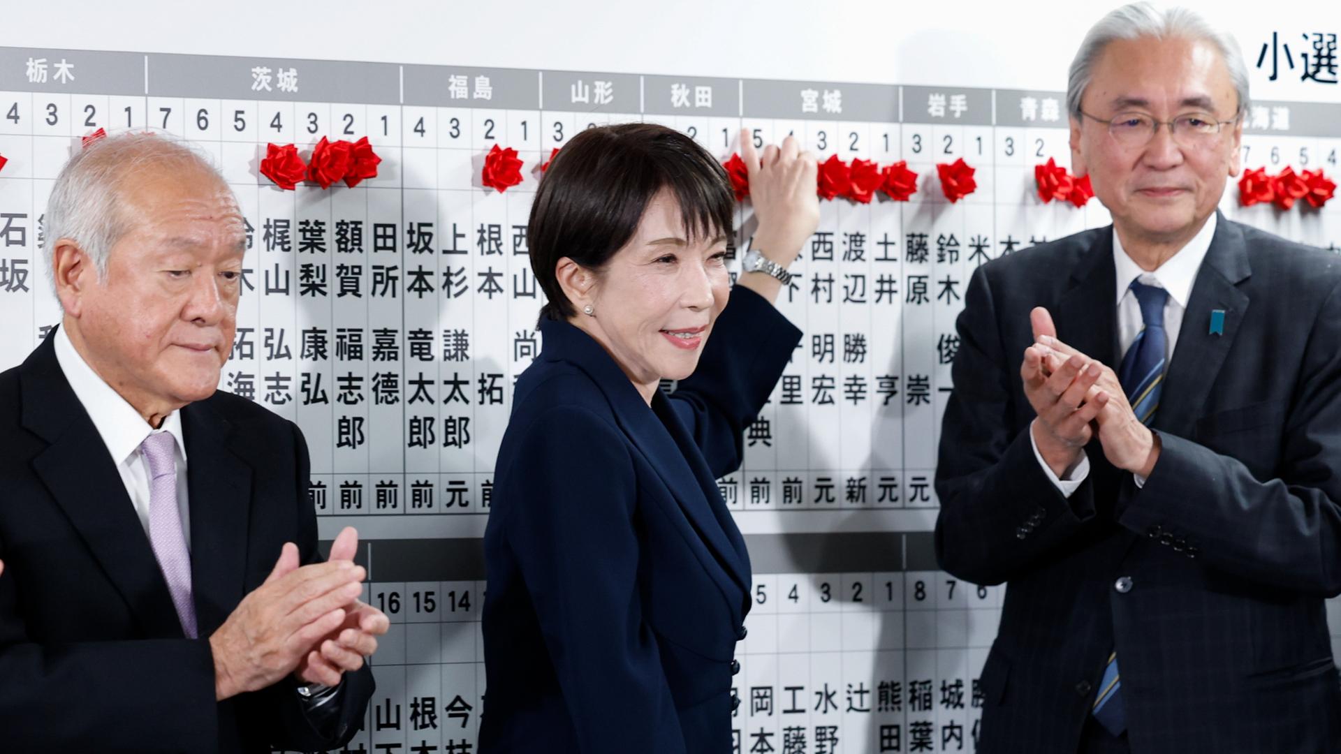 Japans Premierministerin Sanae Takaichi, legt neben LDP-Generalsekretär Shunichi Suzuki und LDP-Wahlkampfstrategiechef Keiji Furuya am Tag der Parlamentswahl im LDP-Hauptquartier in Tokio eine rote Papierrose auf den Namen eines gewählten Kandidaten. | EPA