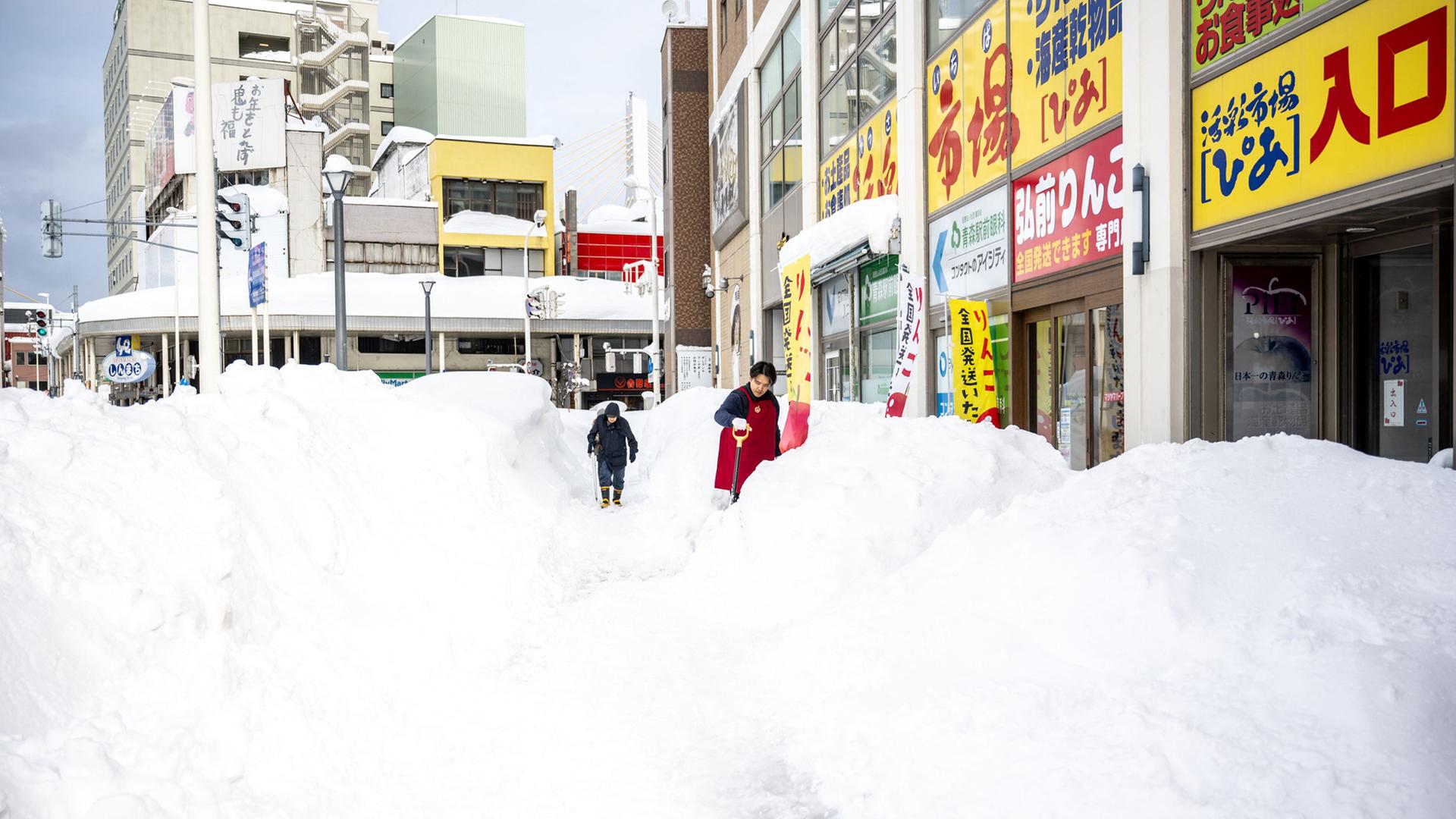 Ein Ladenangestellter schaufelt vor einem Geschäft in der japanischen Stadt Aomori Schnee. | AFP