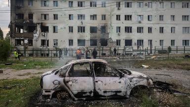 Ein ausgebrantes Auto steht vor einem beschädigten Haus.  
