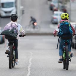 Zwei Schulkinder fahren mit ihren Fahrrädern eine Straße entlang.