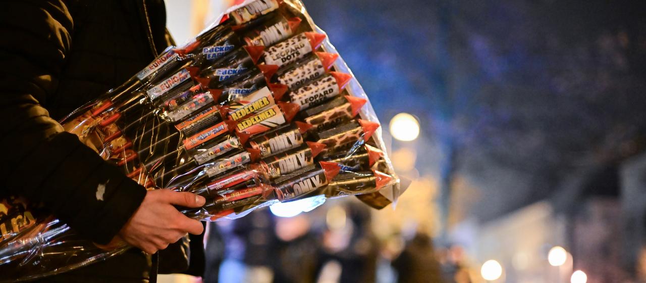 Ein Mann hält Feuerwerks-Raketen unter seinem Arm. 